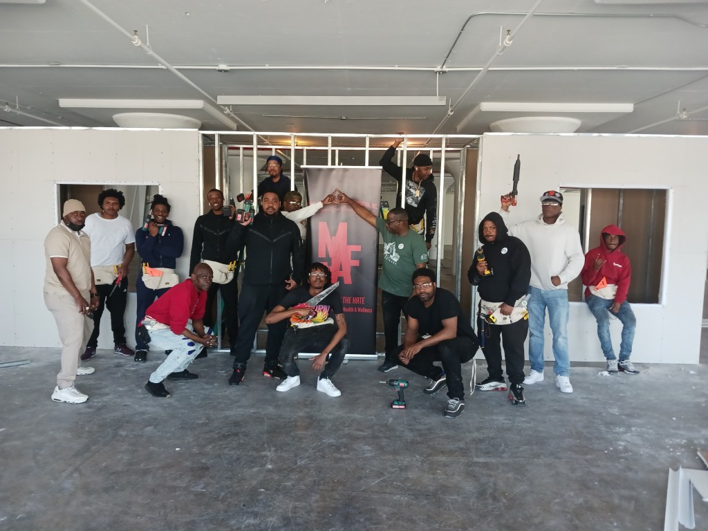 A group of young black men standing in a classroom with a MJAF banner